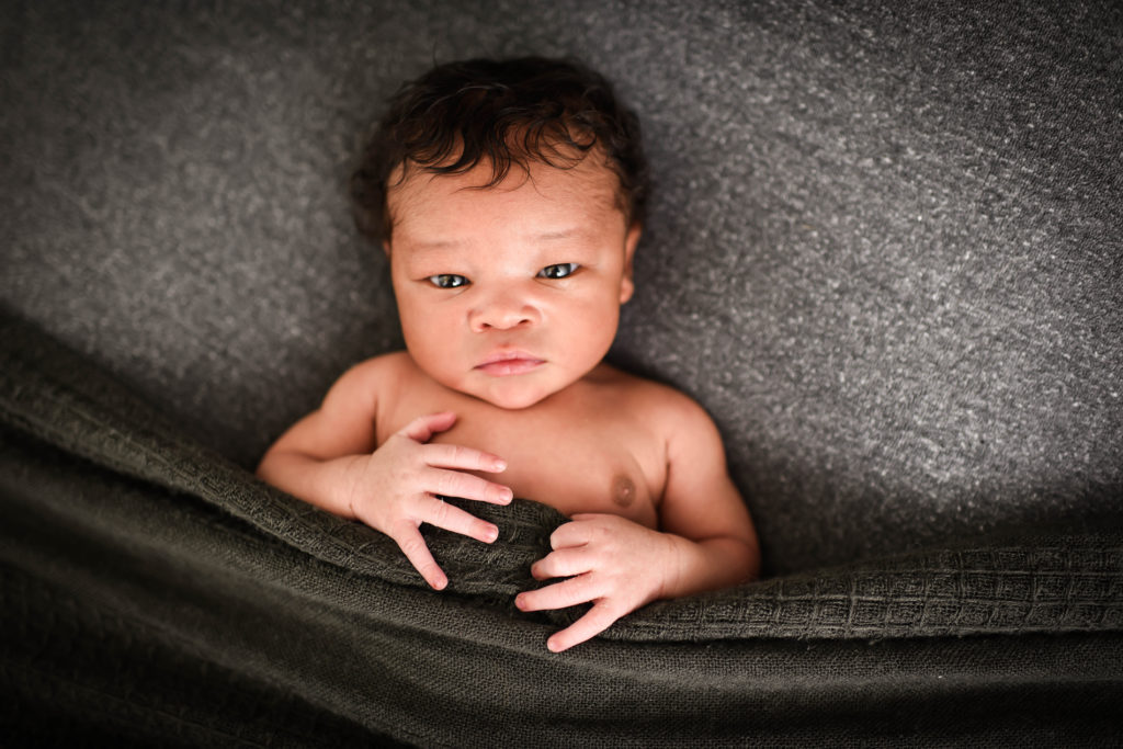 Newborn Photographer, A baby lays awake on a bed under covers.
